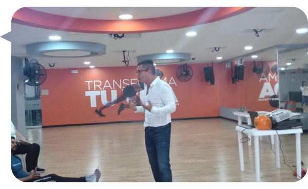 Carlos Sánchez Ortiz impartiendo una conferencia en un gimnasio, motivando a la audiencia sobre la superación personal y el manejo de emociones.