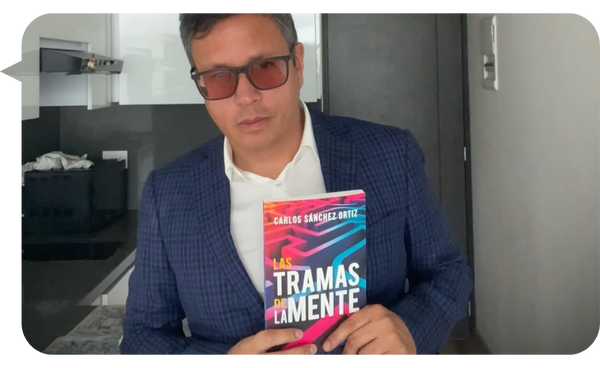 Carlos Sánchez Ortiz sosteniendo su libro "Las Tramas de la Mente", vistiendo un traje formal y gafas.