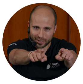 Fotografía de Sergio Hernández en acción durante una conferencia, señalando con ambas manos hacia el público, usando auricular de micrófono y camiseta negra con logotipo de Oli’s Coach