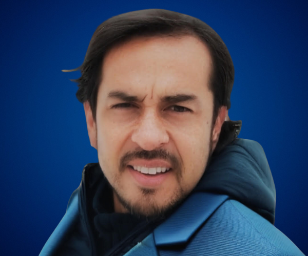 Fotografía de Diego Gómez Villalobos, en primer plano con chaqueta azul y fondo azul intenso, expresión serena y mirada directa a la cámara.